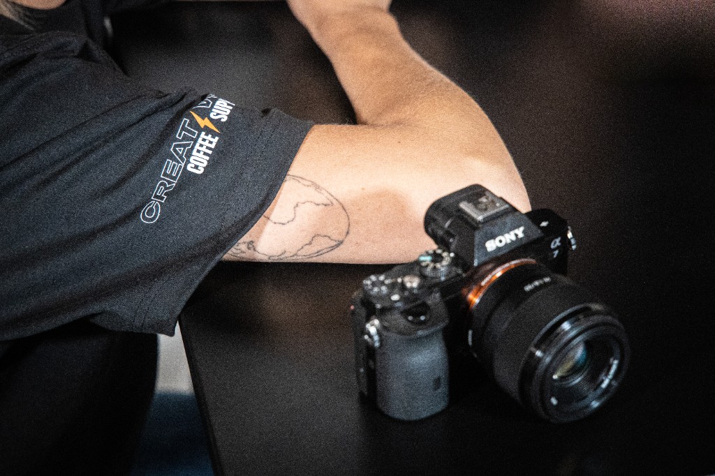 Sony camera beside arm wearing Creative Coffee Supply sleeve logo