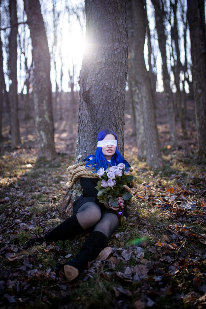 Full-length portrait of blue-haired artist standing in forest